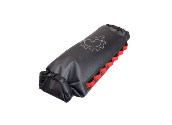 A Revelate Saltyroll bikepacking drybag designed for mounting on a handlebar carrying system is shown in a black waterproof material with two ends with roll-down closures and red daisy chain webbing down the long side