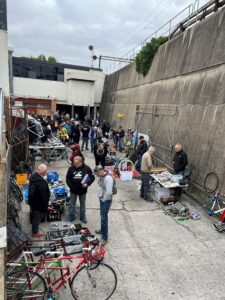 The Bicycle Swap Meet out the back of Abbotsford Cycles is shown with stallholders chatting to market visitors and lots of bicycle components on the stalls