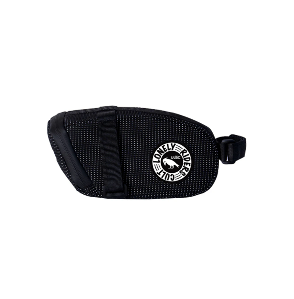 A small oblong shaped black ULAC Radtail Max 1.3L saddle bag is shown with the velcro loop that would mount it to a bicycle seat post attached to the end